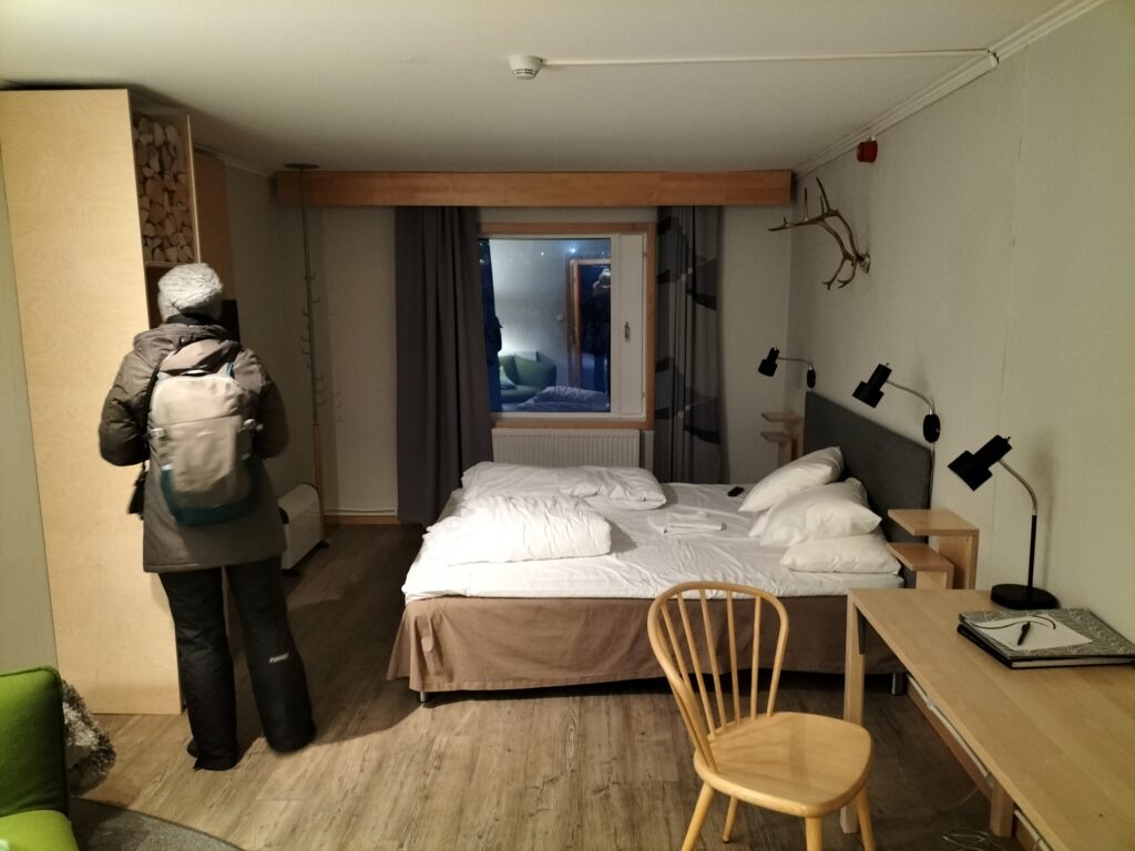 Claudia inside the room at Camp Ripan. A chair in the foreground and the double bed in the background.