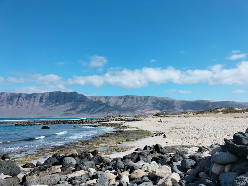 Image of the sea of ​​Famara Beach. In the foreground the stones and in the background the mountains of the island.