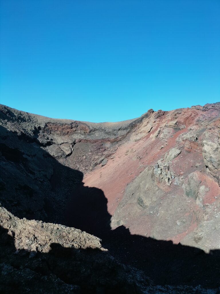 The interior of the volcano with the shadow and shades of red. In the background the blue sky.