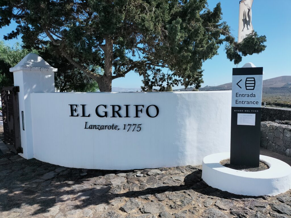 The entrance to the El Grifo winery with a white wall and a tree.