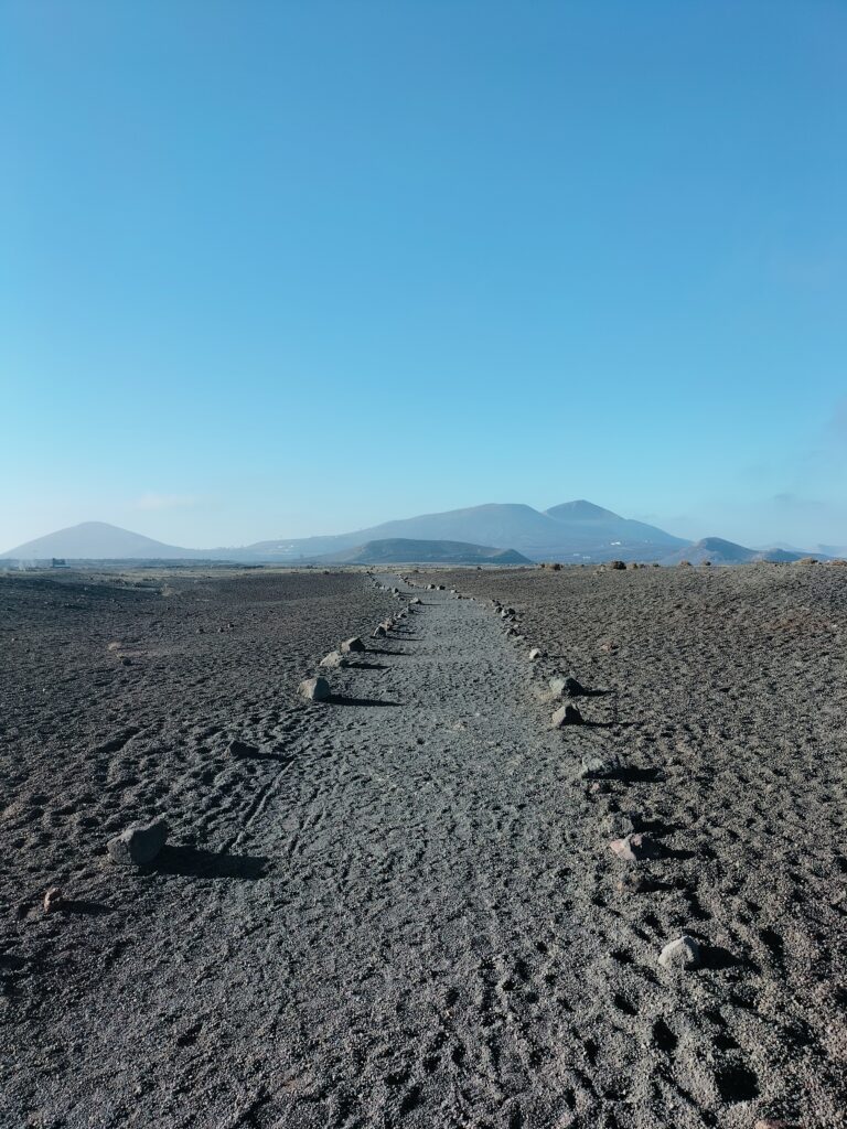 The trek that leads up to the volcano. In the background the mountains and in the foreground the path bordered by small boulders.