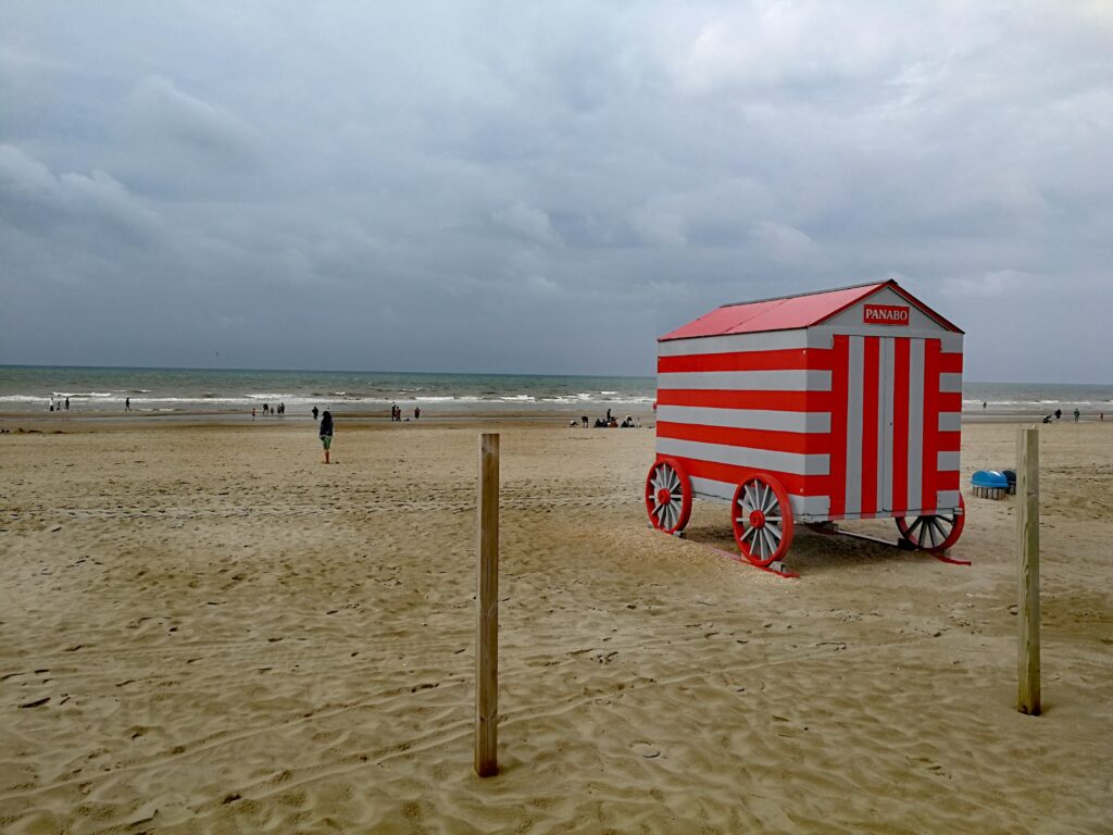 Grey and red colored cabin with wheels on De Panne beach.