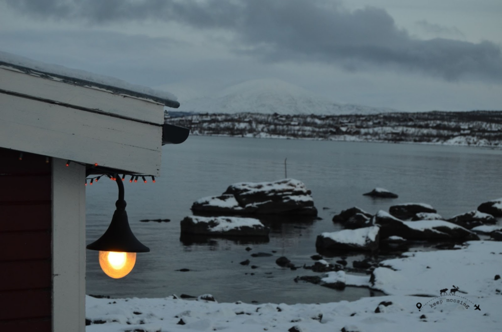 A typical Lappish house with an external street lamp lit, Lake Tornetrask in the background.