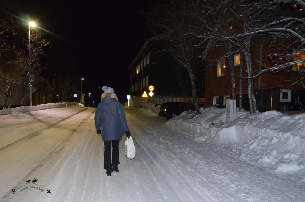 Claudia from behind walking in the snow in the center of Kiruna with a shopping bag in her hand.