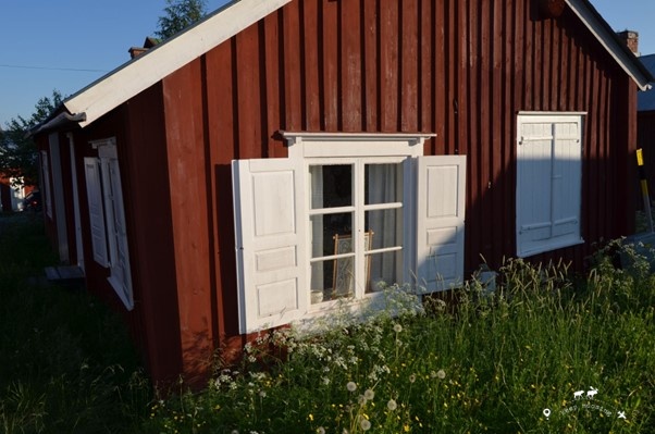 A window with white shutters of a typical Gammelstad house. The garden in the foreground.