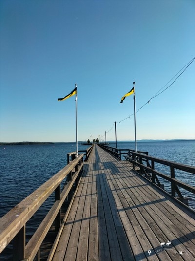 Wooden jetty in the town of Rattvik. Two Swedish flags are flying with the blue sky in the background and the lake around.