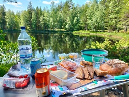 The picnic table laden with food and drinks in front of a pond immersed in the Scandinavian forest..