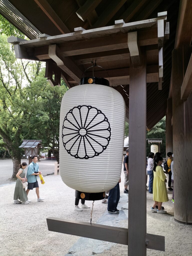 A white lantern with a black wheel painted on it. Tourists in the background.