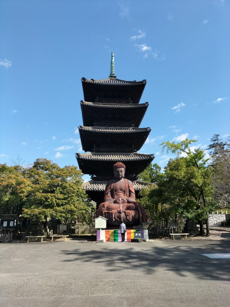 Entrance of Koshoji Temple with a large Buddha statue and a person praying. Behind the statue the five-story pagoda.