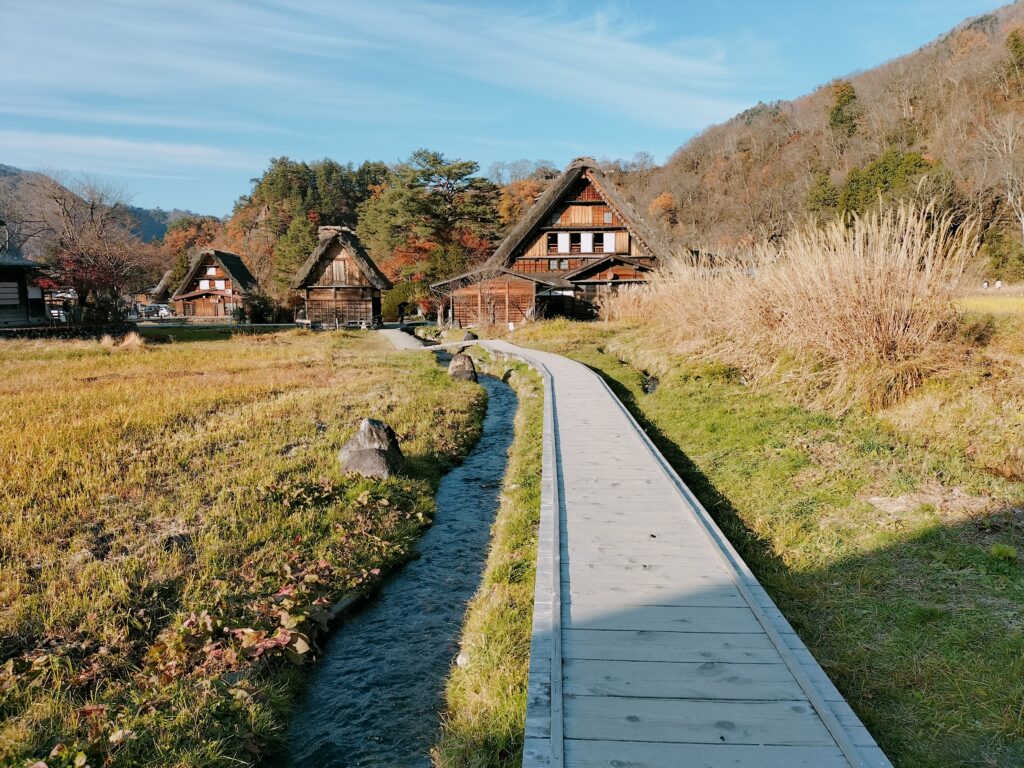 Panorama of Shirakawa-go with the passage and the river in the foreground and some typical houses in the background.