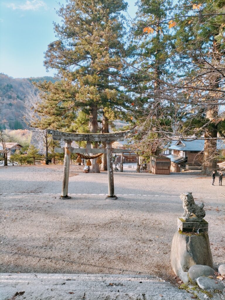 An image of Myozenji Temple with a stone torii in the center and a small statue on the right. The trees in the background.