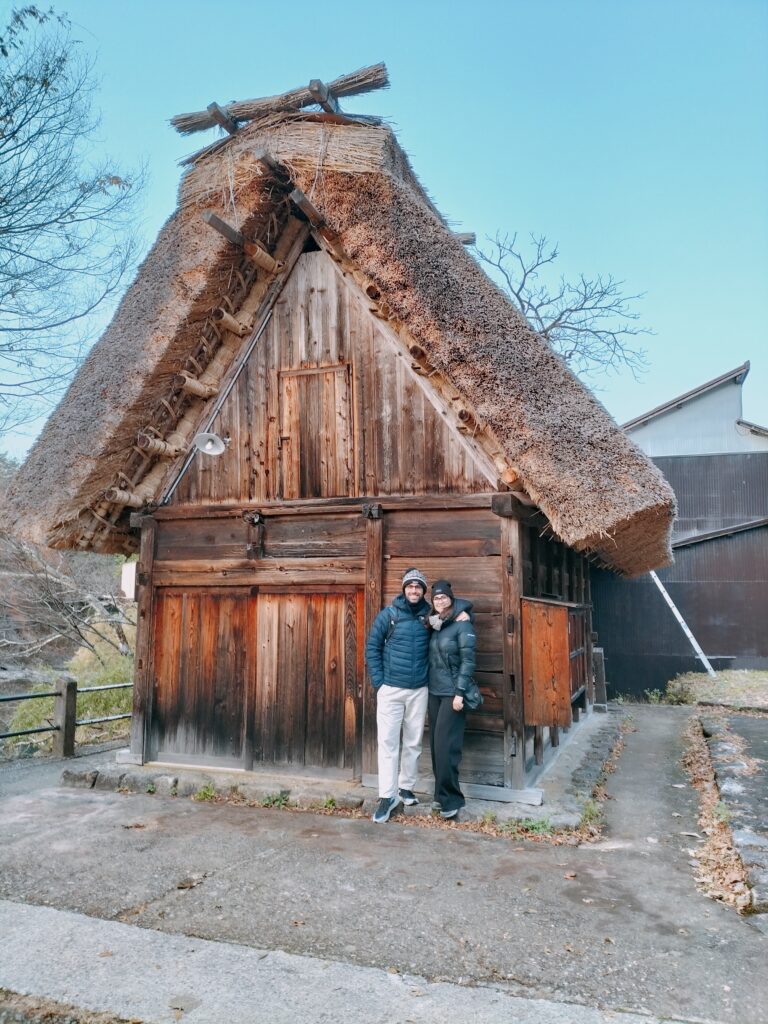 Tiziano and Claudia in front of a typical house with a sloping thatched roof.