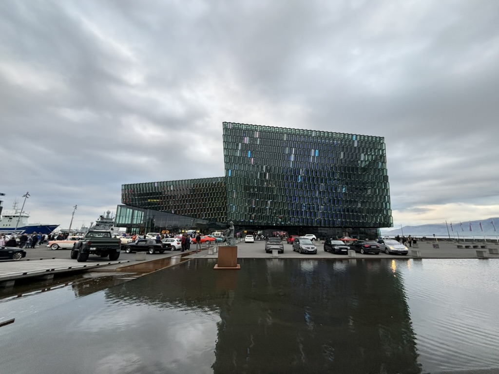 View of the Harpa from the outside with some cars parked.