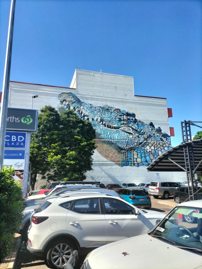 A mural art work of a crocodile. Some cars in the foreground.