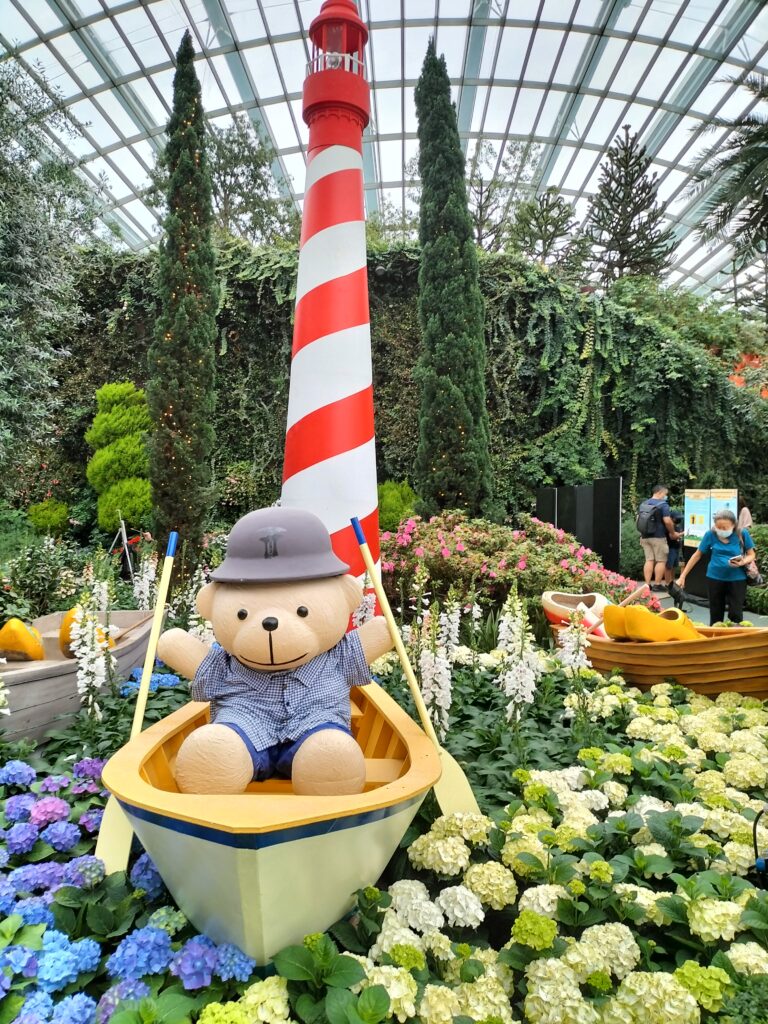 A sculpture with a Teddy Bear on a canoa in a sea of flowers.