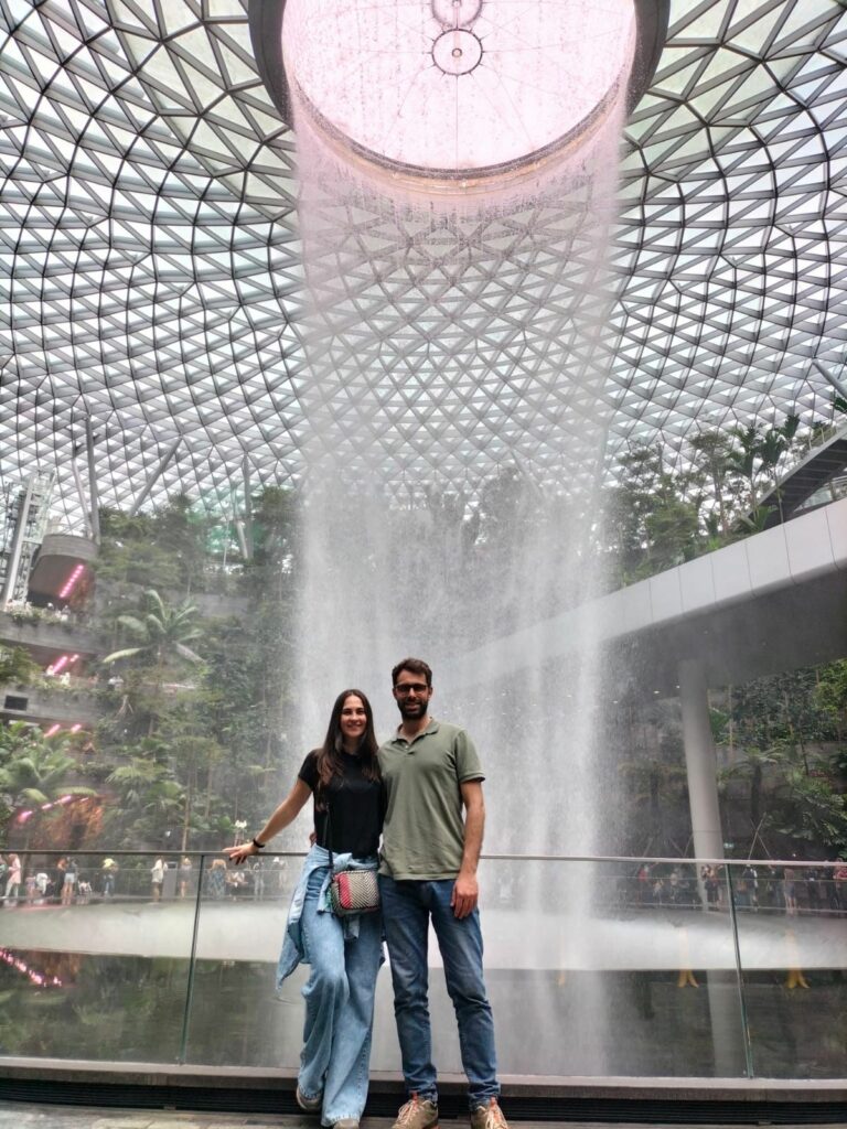 Tiziano and Claudia inside Terminal 4 at Changi Airport in front of the waterfall.